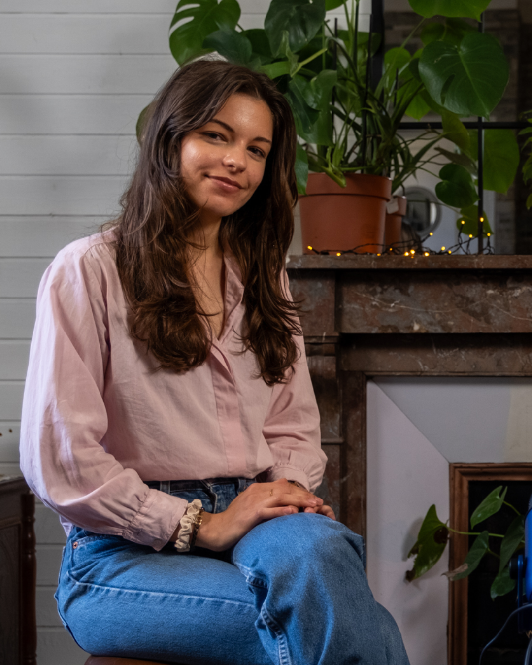 Chiara Costantini, ritratto: è seduta in un ambiente luminoso e guarda in camera con un leggero sorriso; dietro di lei una parete chiara e una grande pianta su un camino